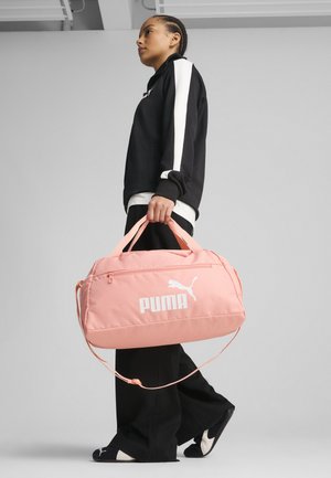Różowa torba sportowa wykonana z miękkiego materiału z białym logo "PUMA", górnymi uchwytami oraz odpinanym paskiem na ramię. Zamek błyskawiczny z przodu.