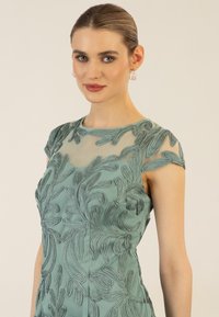 Abito a maniche corte ricamato in un delicato teal, con motivi floreali, sovrapposizione trasparente e design aderente, che mette in evidenza dettagli di cucitura intricati.