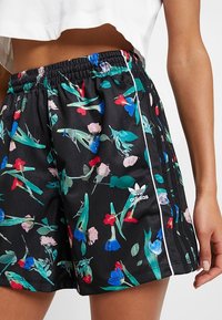 Svarta shorts med ett blommönster som har röda, blå och gröna blommor. Elastisk midja, sidostripes och Adidas-logotyp. Lättvikts tyg.