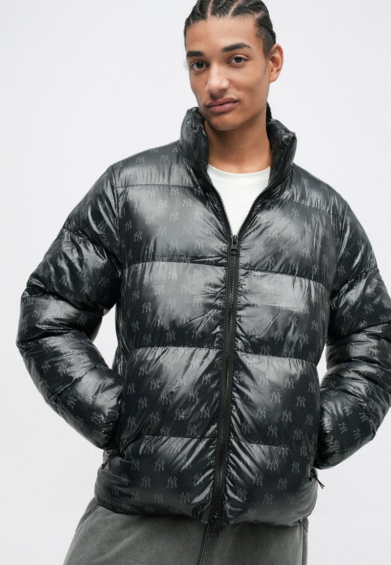 Schwarze Steppjacke mit glänzender Oberfläche, ausgestattet mit horizontalen Steppabschnitten und dezentem Logo-Muster. Hoher Kragen und Frontreißverschluss.