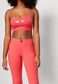 Korallenfarbener gerippter Cropped-Top mit dünnen Trägern und Logo; passende korallenfarbene Leggings mit Logo am Bund. Beide aus elastischem Stoff gefertigt.