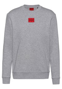Grauer Pullover aus weichem Stoff, mit Rundhalsausschnitt, langen Ärmeln und einem roten quadratischen Logoaufn äher mit schwarzem Text auf der Brust.