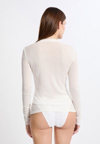 Maglietta a maniche lunghe color crema chiaro, leggera, dalla vestibilità aderente, con una texture morbida e un tessuto liscio. Mutande bianche senza cuciture visibili lungo il bordo inferiore.