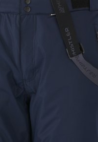 Marinblå skidbyxor med en slät, vattenavvisande tyg, som har två knappar, en logotypetikett och justerbara svarta remmar med 'HISTLER' präglat.