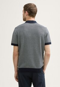 Polo shirt rayé bleu marine et blanc avec un col et des poignets côtelés, des manches courtes et un design en tricot texturé.