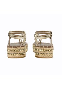 Sandali dorati con cinturini, dotati di una base piattaforma, caratterizzati da juta intrecciata e piccole borchie metalliche. Parte superiore liscia e plantare texture.