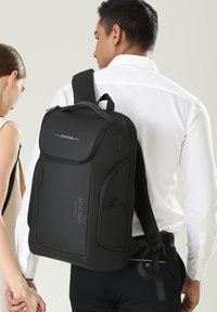 Zaino nero con più cerniere, pannello posteriore imbottito, spallacci regolabili e dettagli con logo. Materiale liscio con forma rettangolare.
