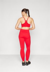 Rød atletisk sports-BH og høyde-liv leggings, begge laget av tøyelig stoff. BH-en har racerback-design; leggingsene sitter tett.