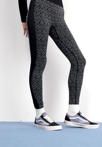 Leggins negros con un diseño geométrico, que presentan una textura suave y paneles laterales en contraste. Combinados con zapatillas negras y moradas.