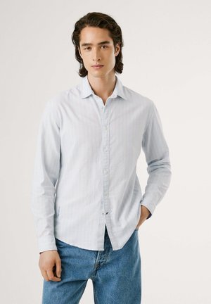 Hellblaues Langarmhemd mit vertikalen weißen Streifen, Knopfleiste und weichem Stoff. Getragen mit blauen Jeans.