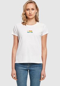 White cotton t-shirt featuring a multicolored "LOVE" embroidered design at the center. Short sleeves and a relaxed fit, paired with light blue jeans.