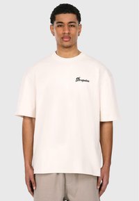 Kortærmet creme t-shirt lavet af bomuld, med en afslappet pasform og et lille mørkt logo på venstre brystområde. Glat tekstur.