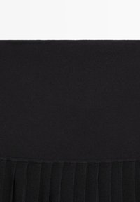 Gonna nera con una parte superiore aderente e una parte inferiore plissettata. Il materiale sembra liscio con una texture morbida in tutta la superficie.