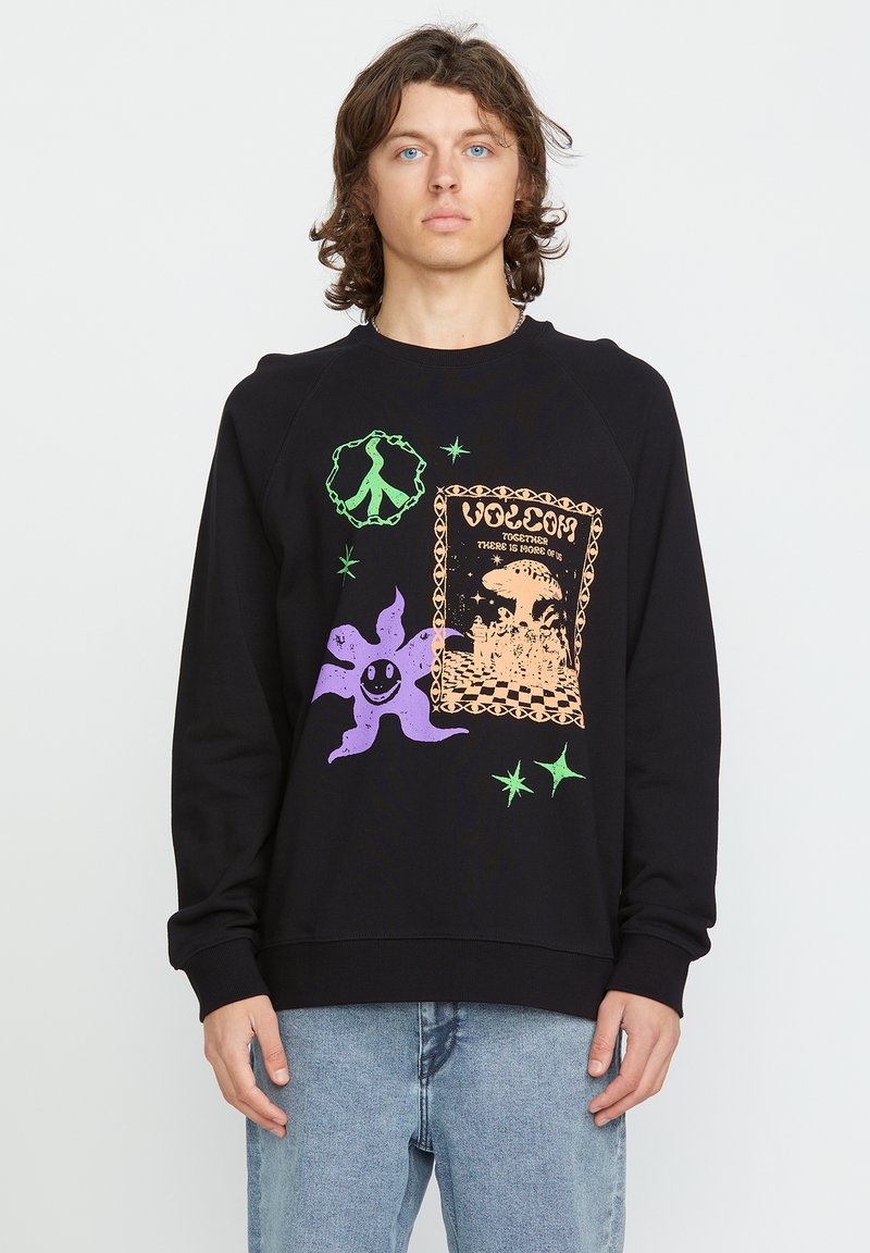 Sweatshirt noir avec des graphiques colorés, y compris un personnage souriant violet, un symbole de paix et un design décoratif. Présente des poignets côtelés.
