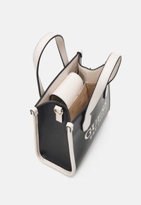 Sac à main noir et crème au design structuré, avec un logo, des poignées courtes et une poche intérieure pour l'organisation.