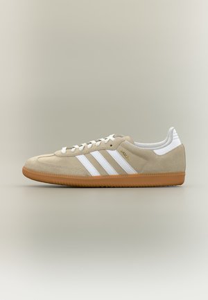 Beige suede low-top sneaker with white laces, white stripes on the side, gum sole, and "SAMBA" printed in gold lettering.