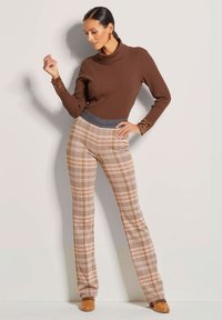 Brown ribbed turtleneck top with lace accents, paired with beige plaid trousers featuring orange and brown patterns, completed with tan shoes.