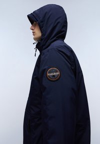 Marineblauwe hooded jack met een ritssluiting aan de voorkant, textuurstof en een rond logo-op-niveau op de linker mouw. Voorzien van een verstelbare capuchon en zakken.