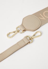 Cintura in pelle beige con dettagli in oro, inclusa una gancio a scatto. Materiale testurizzato e dettaglio logo impresso su una striscia di tessuto più ampia.