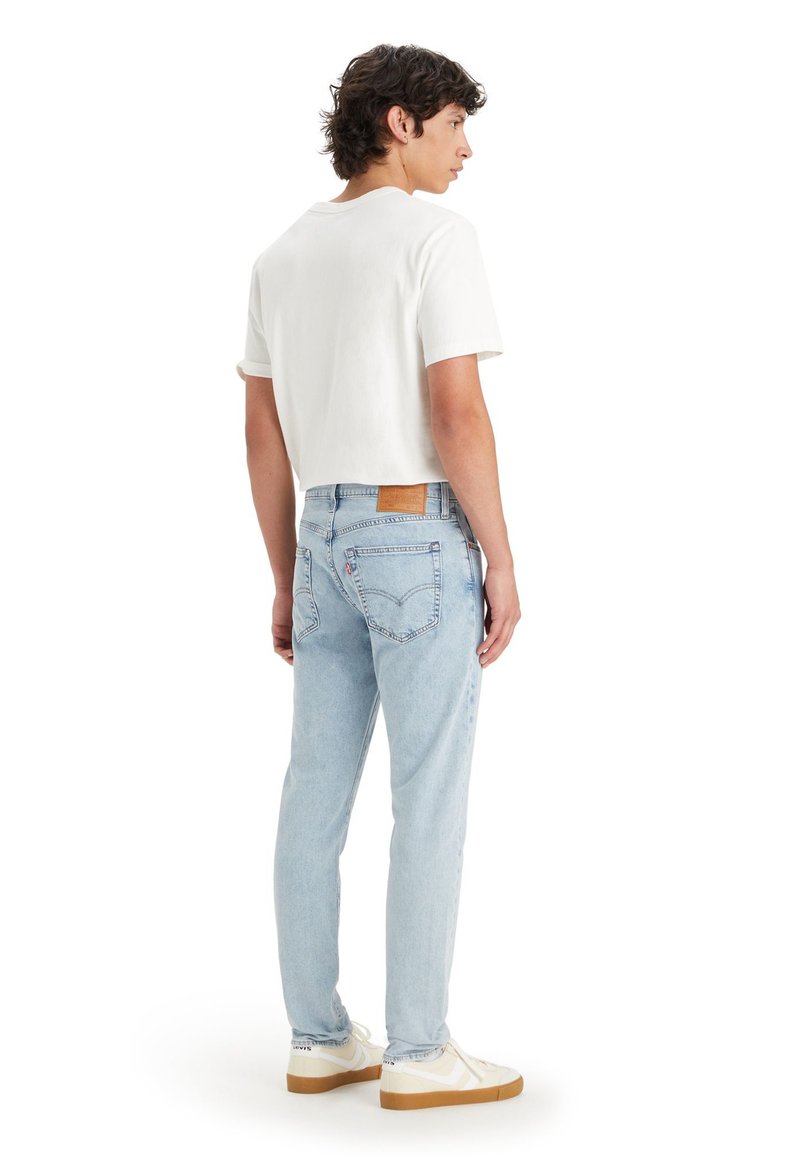 Ljusblå denimjeans med tapered passform, med en brun läderlapp på baksidan, stilade med en vit kortärmad skjorta.