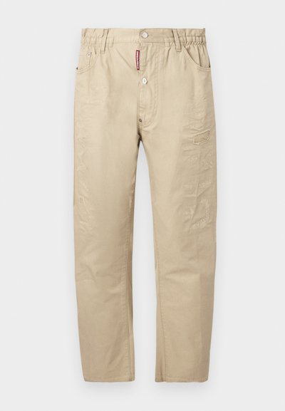 Pantalon décontracté beige avec ceinture élastique, bouton et fermeture éclair à l'avant, poches latérales, détails de couture subtils et une étiquette logo rouge au niveau de la braguette.