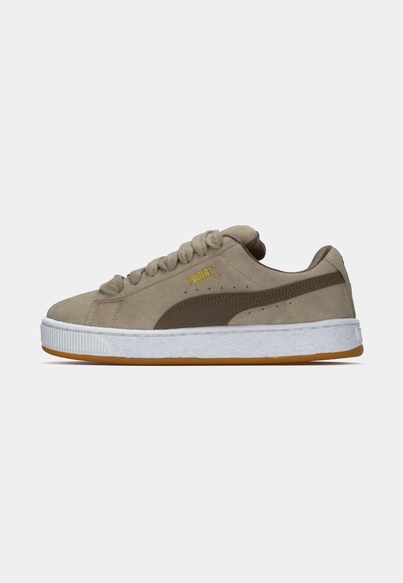 Zapatillas de ante en beige con suela de goma blanca. Presentan acentos marrones, superficie texturizada y cordones redondos. Logotipo dorado en el lateral.