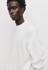 Hvid sweatshirt med rund halsudskæring, oversized pasform og blød tekstur. Enkel design uden synlige mønstre eller hardware detaljer.