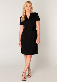 Zwarte jurk met korte mouwen, een V-hals en een taille met ceintuur. Gemaakt van gladde stof, het heeft een relaxte pasvorm en een zoom tot op de knie met zijslits.