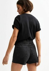 Camiseta negra de manga enrollada combinada con pantalones cortos de mezclilla negra de cintura alta. Los pantalones cortos tienen un dobladillo deshilachado y dos bolsillos traseros.