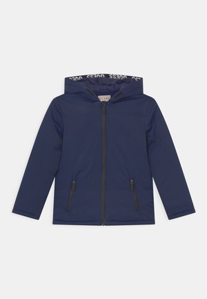 Veste à capuche bleu marine avec fermeture éclair à l'avant, deux poches zippées et doublure marquée "GUESS" à l'intérieur de la capuche, présentée sur fond blanc.