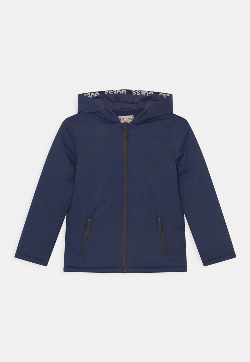 Veste à capuche bleu marine avec fermeture éclair à l'avant, deux poches zippées et doublure marquée "GUESS" à l'intérieur de la capuche, présentée sur fond blanc.