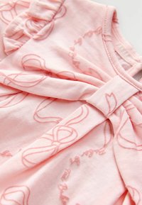 Top rosa chiaro realizzato in morbido cotone, con un delicato motivo a fiocchi, maniche arricciate e un dettaglio arricciato sul collo.