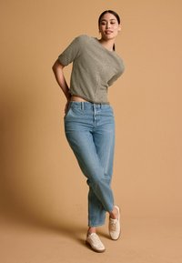 Top scurt texturat de culoare verde măslin, cu mâneci scurte, asortat cu blugi cu talie înaltă de culoare albastră deschisă și adidași de culoare crem.