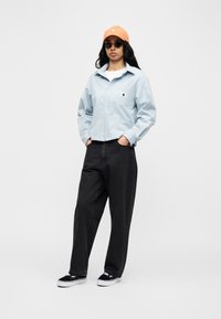 Ανοιχτό μπλε, πουκάμισο με σχέδια και γιακά, μαύρο παντελόνι, μαύρα αθλητικά παπούτσια και πορτοκαλί καπέλο. Τα γυαλιά ηλίου ολοκληρώνουν το καθημερινό ντύσιμο.