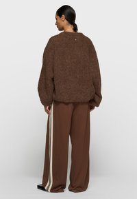 Brauner flauschiger Pullover mit lockerem Sitz und rundem Ausschnitt. Kombiniert mit lockeren braunen Hosen, die vertikale cremefarbene Streifen haben.