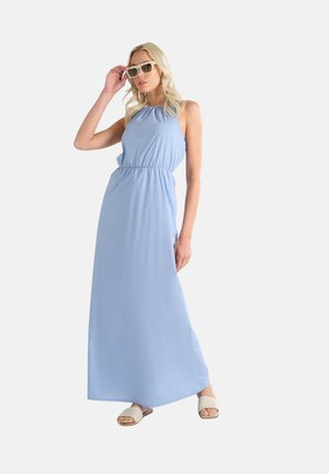 Maxi dress azzurro chiaro con scollatura a halter, vita elastica e tessuto morbido; abbinato a occhiali da sole bianchi e sandali beige.