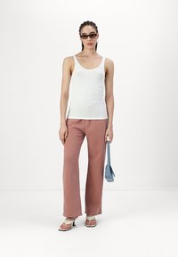 Top sin mangas blanco, pantalones de pierna ancha rosa y sandalias blancas con tiras. Los accesorios incluyen un pequeño bolso azul y gafas de sol de estilo retro en negro.