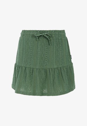 Weißes ärmelloses Oberteil mit Rüschen an den Schultern, kombiniert mit einem grünen Stufenrock mit strukturiertem Muster. Schwarze Sandalen runden das Outfit ab.