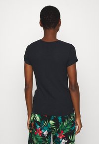 Sort ribbet t-shirt med korte ærmer og rund hals, parret med mønstrede tropiske bukser med store grønne blade og lyse blomster.