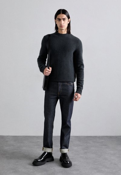 Pull en maille gris foncé, jeans en denim avec revers et chaussures en cuir noires. Les accessoires comprennent un sac à bandoulière noir. Design simple, style décontracté.