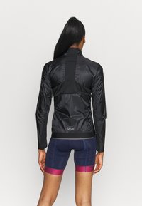 Czarna, lekka kurtka z długimi rękawami, wysokim kołnierzem i odblaskowymi akcentami. Materiał ma gładką fakturę. Logo na plecach.