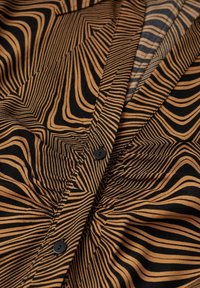 Tissu à motifs bruns et noirs avec des lignes ondulées, doté d'une fermeture à bouton et d'une légère texture. Détail en gros plan du vêtement.