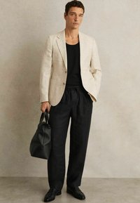 Fakó bézs vászon zakó, fekete bordás top alatt, laza fekete nadrággal és fekete bőr cipővel párosítva. Egy fekete táska az egyik kézben.