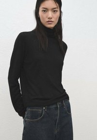 Pulover negru cu guler înalt, realizat dintr-un material moale, design mulat, mâneci lungi, asortat cu blugi cu talie înaltă, de culoare albastru închis. Stil simplu, minimalist.