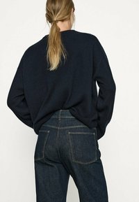 Mörkblå stickad tröja med avslappnad passform, tillsammans med mörka denimjeans med kontrasterande sömmar och två bakfickor.