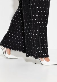 Zwart geplooid maxi-jurk met witte stippen, met een rucheszoom. Gepaard met witte puntige hakken met transparante accenten.