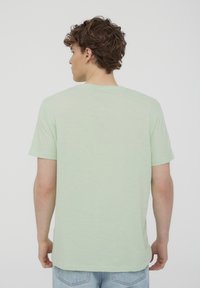 T-shirt verde chiaro a maniche corte realizzato in un tessuto morbido e testurizzato. Collo rotondo e vestibilità rilassata, con una parte posteriore semplice.