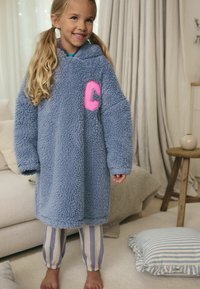 Uldet blå hætteplade med et pink "C"-mærke, der har løse ærmer og en bred krop. Båret over stribede pyjamasbukser.