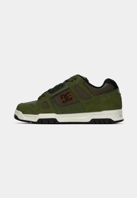 Green suede sneaker with a white rubber sole, featuring black accents, perforated panels, and an orange logo on the side.