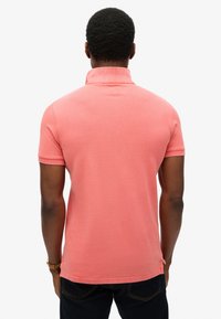 Camisa polo ajustada en color coral, de manga corta, con cuello de canalé, confeccionada en una tela suave con una textura sutil. Aberturas laterales en el dobladillo.